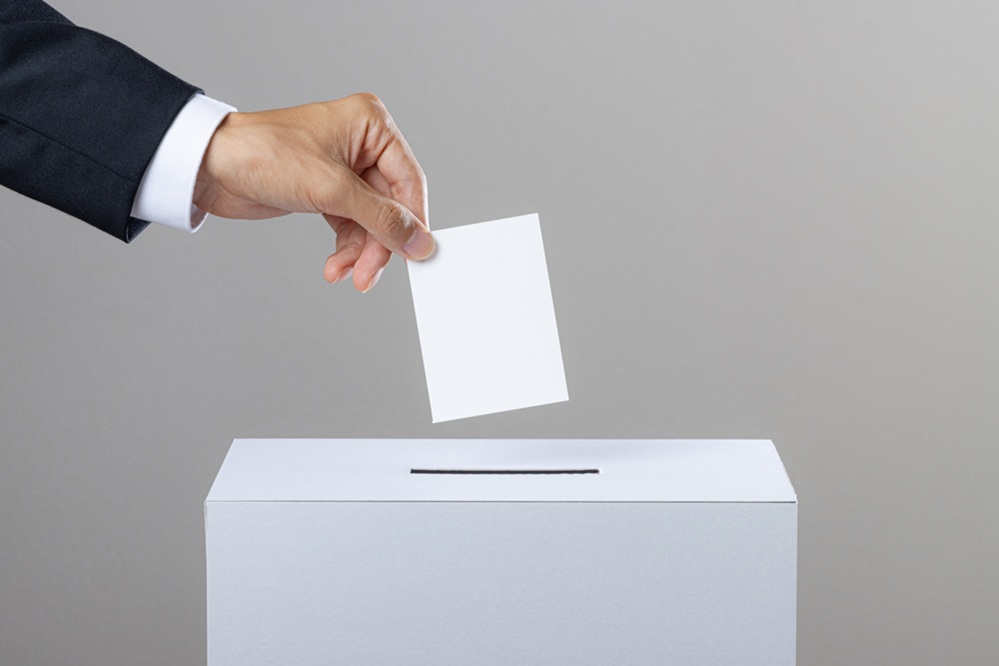 白い投票箱と投票用紙を投票しようとしている手